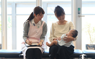 写真：赤ちゃんを抱くお母さんと記録をとる人