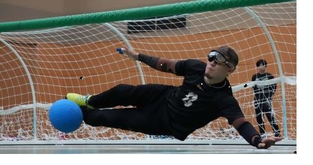 男性キーパーがシュートを止めようとボールに向かって飛んでいる